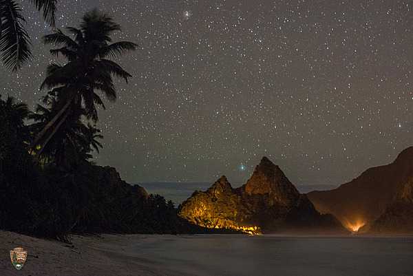 Secluded Ofu sand beach at night. The island of Olosega rises in the distance at far right. Photo courtesy of the US National Park Service.