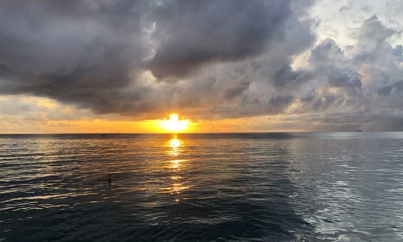 At sunset, the west coast of Barbados offers beautiful sunsets and calm waters. A cruise ship may be seen departing Barbados as a swimmer watches the sun drop over the horizon.