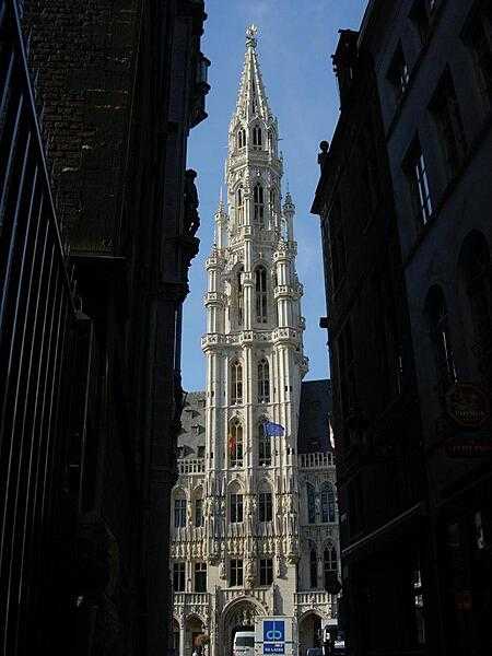 The imposing main tower of the Hotel de Ville/Stadhuis (City Hall) in Brussels. Built in the Gothic style, parts of the structure date back to the early 15th century. Its spire is topped by a gilt metal statue of the Archangel Michael, patron saint of Brussels. The facade is decorated with statues of nobles, saints, and allegorical figures.