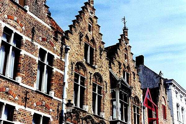 Weather vanes, tall windows, and distinctive roof lines along a Brugge canal.