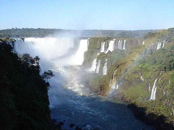The majestic Iguaçu Falls (Iguazú Falls) on the Brazil-Argentine border. The falls are part of a nearly virgin jungle ecosystem surrounded by national parks on both sides of the cascades. The Iguazu River begins in Parana state of Brazil, then crosses a 1,200-km (750 mi) plateau before reaching a series of faults forming the falls.