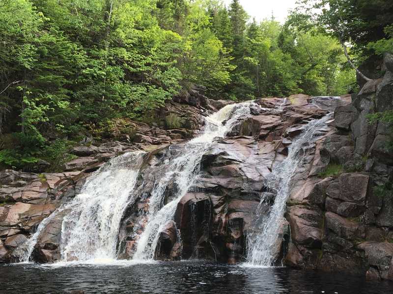 A paved pathway leads to the iconic Mary Ann Falls near Cape Breton Highlands National Park, Nova Scotia. Hikers climb the rocks to jump into the pool below.