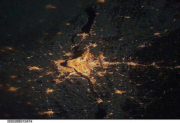 A night view of the Montreal metropolitan area is featured in this image from the International Space Station. This photo of the Montreal, Quebec  metropolitan area (center) illustrates the extent of urbanization made clearly visible by city lights at night. Major roadways and industrial areas are traced by bright white lighting, while the adjacent residential and commercial land uses are characterized by more diffuse yellow-gold lighting. Rivers and other water bodies appear black, while the surrounding rural countryside is faintly illuminated by moonlight. Blurry areas at top and bottom left are caused by cloud cover. Montreal is the largest city in the dominantly French-speaking province of Quebec, and the second-largest in Canada, after Toronto. While the city of Montreal proper is located on - and almost completely covers - the Island of Montreal at the confluence of the St. Lawrence (center) and Ottawa Rivers (not visible), the city takes its name from Mont Royal located at the city&apos;s center. Image courtesy of NASA.