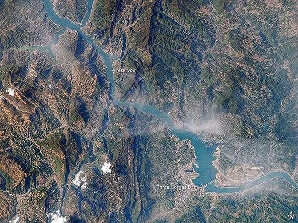 An image from 15 April 2009 showing the Three Gorges Dam on the Yangtze River and the flooding upriver from the dam. The main purposes for the dam are twofold: to supply water for the largest hydroelectric plant in the world and to help control the devastating floods that plague the lowlands downstream from the dam. The epic scale of the dam project is matched by the level of controversy it continues to generate. Concerns about major environmental impacts, the relocation of 1.3 million people, and the flooding of 13 cities, more than 1,300 villages, archeological locations, and hazardous waste dumps were raised throughout the planning and implementation. Environmental concerns include increased seismicity from the loading of the water, landslides, changed ecosystems, accumulated pollution, increased chances for waterborne diseases, and salinity changes in the Yangtze estuary. Photo courtesy of NASA.