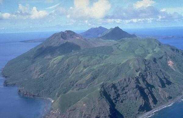 Aerial view of Pagan Island looking northeastward. South Pagan volcano (left) occupies the southwest end of Pagan Island. The ridge in the right foreground is the eroded rim of a 4-km-wide caldera inside which the conical South Pagan volcano was constructed. The elongated summit of South Pagan is cut by four craters. Eruptions of South Pagan volcano occurred during the 19th century, but it has been much less active than North Pagan volcano, the peak at the far center on the northeast tip of the island. Image courtesy of the US Navy.