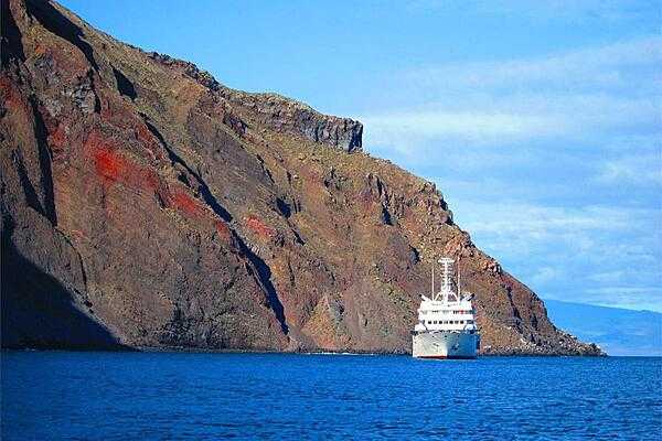 A cruise ship beside a color-streaked cliff in Punta Vicente Roca on Isabela Island.