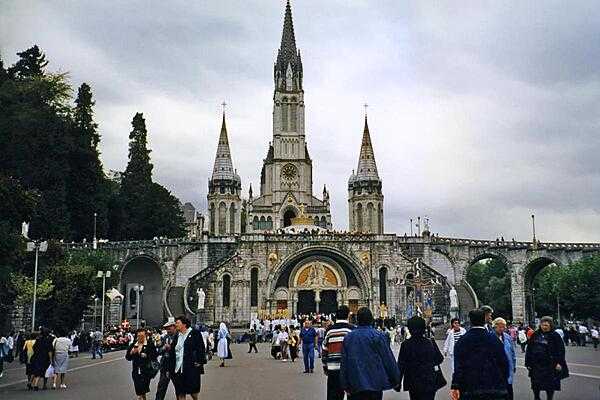 Pilgrims and visitors at Lourdes. The Rosary Basilica in the foreground serves as an entranceway to the larger Basilica of the Immaculate Conception behind. Lourdes is the reputed site of 18 Marian apparitions in 1858. The town is one of the world&apos;s greatest pilgrimage sites hosting some 5 million visitors annually.