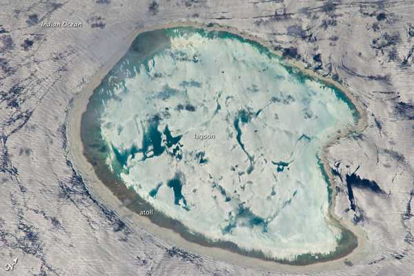This photograph of Bassas da India, an uninhabited atoll in the îles Eparses group of the Indian Ocean, has an almost surreal quality due to varying degrees of sunglint. Sunglint is caused by light reflecting off a water surface directly back towards the observer. Variations in the roughness of the water surface - the presence or absence of waves due to wind and currents - will cause differences in the intensity of the sunglint. In this image, the presence of currents is highlighted as darker patches or streaks (image left and upper right). In contrast, shallow water in the lagoon presents a more uniform, mirror-like appearance, suggesting that there are no subsurface currents. Photo courtesy of NASA.