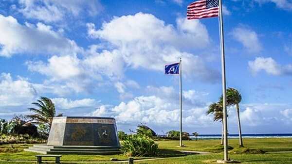 A hexagonal monument, dedicated in 1994 on the 50th anniversary of the liberation of Guam, stands at the War in the Pacific National Historical Park under the flags of the United States and Guam. The monument's inscription reads: "Honors to heroic and gallant effort of the US Armed Forces". Photo courtesy of the US National Park Service.