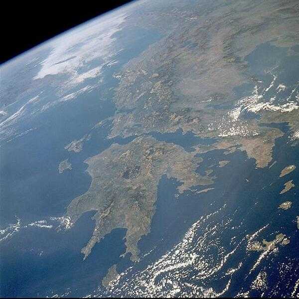 This northwest-looking photo displays the rugged, mountainous landscape of Greece. Two major landform regions are captured in the photo - the northwest-southeast-trending Pindus Mtns. in central Greece north of the Gulf of Corinth and the Peloponnese Peninsula south of the Gulf (center of the photo). This rugged terrain caused the Greeks to become a seafaring people, second only to the Norwegians in Europe. The capital of Athens (lighter area) is barely discernible along the southern edge of the broad peninsula near the eastern edge of the photograph. Image courtesy of NASA.