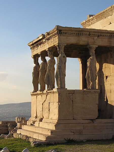 The south side of the Erechtheion with the "Porch of the Maidens," composed of six draped female figures (caryatids) as supporting columns. One of the six figures was removed in the early 19th century and is now in the British Museum in London; it was replaced by a copy. The Acropolis Museum in Athens holds the remaining original five figures, which have been replaced onsite by replicas.