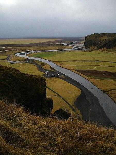 A river with volcanic black sand banks meanders to the sea through farm fields near the southern coast of Iceland.
