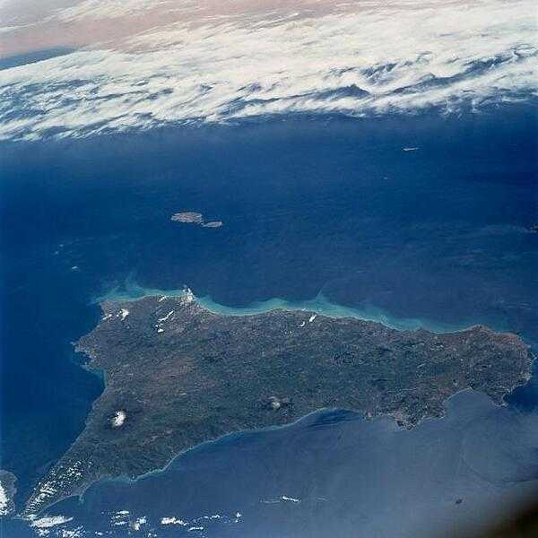 This southerly-looking view taken from onboard the space shuttle, shows the triangular-shaped island of Sicily. With only very limited coastal plains, the island&apos;s topography consists of rugged hills and low mountains. Snow-capped Mt. Etna is visible near the northeast point of the island. Some other distinctive features in this image are the lighter-colored zone of suspended sediment in the water along the southern coast, in the middle distance, the smaller islands of Malta, and off to the south, across the Mediterranean, the north African shore. Image courtesy of NASA.