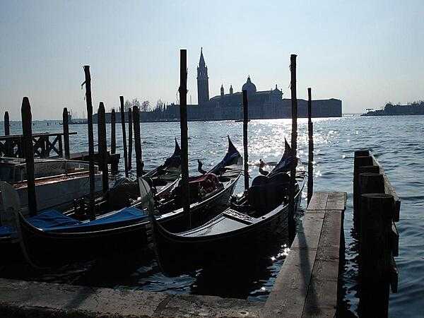 A view of San Giorgio Maggiore Island in Venice across the sparkling waters of the lagoon with gondolas in the foreground.