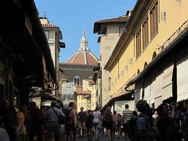 View on the Ponte Vecchio (Old Bridge) with shops (mostly jewelry boutiques) lining the roadway and the dome of the Duomo (Cathedral) in the background.
