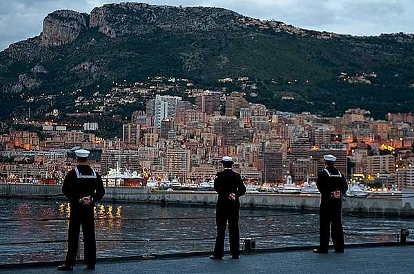 Sailors stationed aboard the amphibious command ship USS Mount Whitney man the rails as the ship arrives in Monaco for a port visit to participate in Monaco's National Day celebration in 2008. Much of Monaco is visible in the background and consists of the built-up area along the coast. Photo courtesy of the US Navy/ Petty Officer