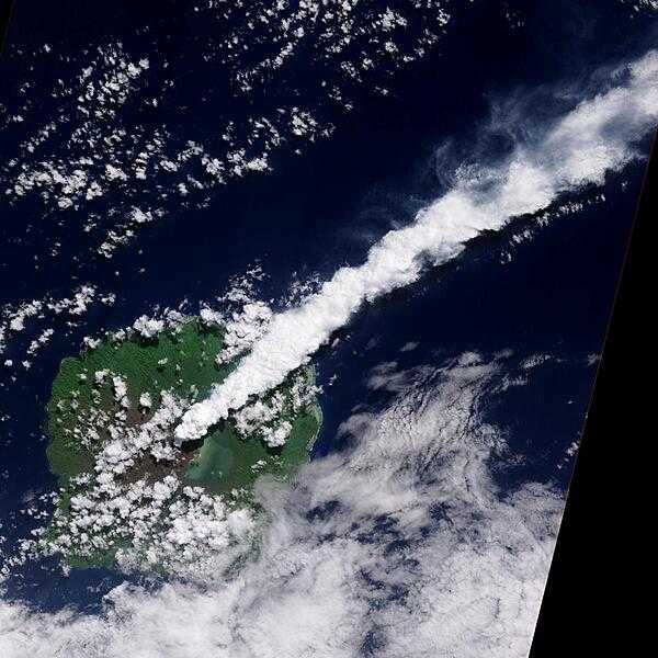 The thick, steam-rich plume from Guau Volcano blows directly northeast in this natural-color satellite image acquired on 24 April 2010. The thick steam is brighter white than the surrounding lower-altitude clouds. Vegetation is green, as is Lake Letas. Vegetation to the south and west of the volcano, damaged by ash and acidic volcanic gases, is dark gray-brown. Photo courtesy of NASA.