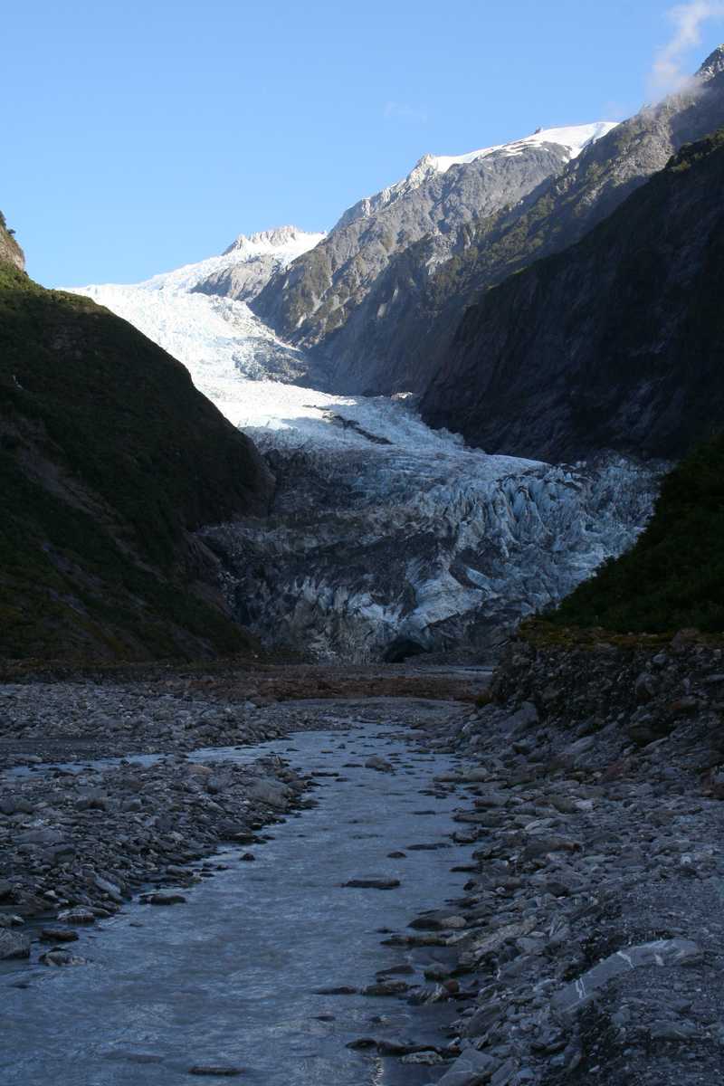 On the South Island’s west coast, two glaciers from the Southern Alps discharge into a coastal river. Fox Glacier has a steep but straight flow from the mountain bowl down to sea level where it forms a glacial river.