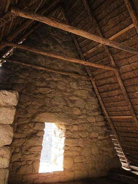 The inside of a Machu Picchu house with a thatched roof showing the traditional shape of Inca windows.