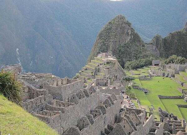 A section of housing is seen in front of Machu Picchu&apos;s Sacred Plaza, with the Intiwatana (Hitching Post of the Sun) above the plaza and the Western Urban Section to its right, where llamas roam.