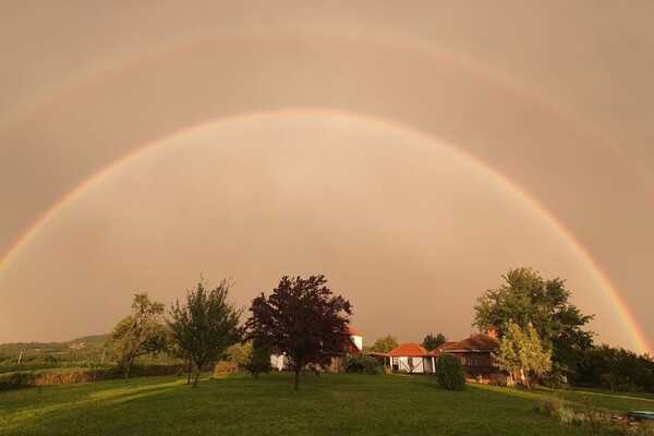A Serbian farmhouse in the countryside under a double rainbow.
