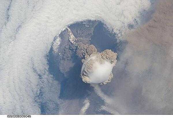 A fortuitous orbit of the International Space Station allowed the astronauts to take this striking view of Sarychev Peak volcano (Russia&apos;s Kuril Islands, northeast of Japan) in an early stage of eruption on 12 June 2009. Sarychev Peak is one of the most active volcanoes in the Kuril Island chain and is located on the northwestern end of Matua Island. Prior to 12 June, the last explosive eruption had occurred in 1989 with eruptions in 1986, 1976, 1954, and 1946 also producing lava flows. 

This detailed photograph is exciting to volcanologists because it captures several phenomena that occur during the earliest stages of an explosive volcanic eruption. The main column is one of a series of plumes that rose above Matua Island on June 12. The plume appears to be a combination of brown ash and white steam. The vigorously rising plume gives the steam a bubble-like appearance; the surrounding atmosphere has been shoved up by the shock wave of the eruption. The smooth white cloud on top may be water condensation that resulted from rapid rising and cooling of the air mass above the ash column, and is probably a transient feature (the eruption plume is starting to punch through). 

The structure also indicates that little or no shearing winds were present at the time to disrupt the plume. By contrast, a cloud of denser, gray ash - most probably a pyroclastic flow - appears to be hugging the ground, descending from the volcano summit. The rising eruption plume casts a shadow to the northwest of the island (bottom center).

Brown ash at a lower altitude of the atmosphere spreads out above the ground at upper right. Low-level stratus clouds approach Matua Island from the east, wrapping around the lower slopes of the volcano. Only about 1.5 km (1 mi) of the coastline of Matua Island (upper center) can be seen beneath the clouds and ash. Image courtesy of NASA.