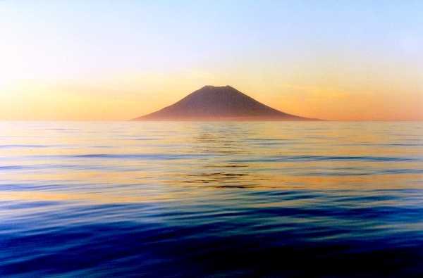Atlasov Island, a symmetrical volcanic cone in the Kuril Island chain, meets the dawn over a calm North Pacific Ocean. Photo courtesy of NOAA / Anatoly Gruzevich.