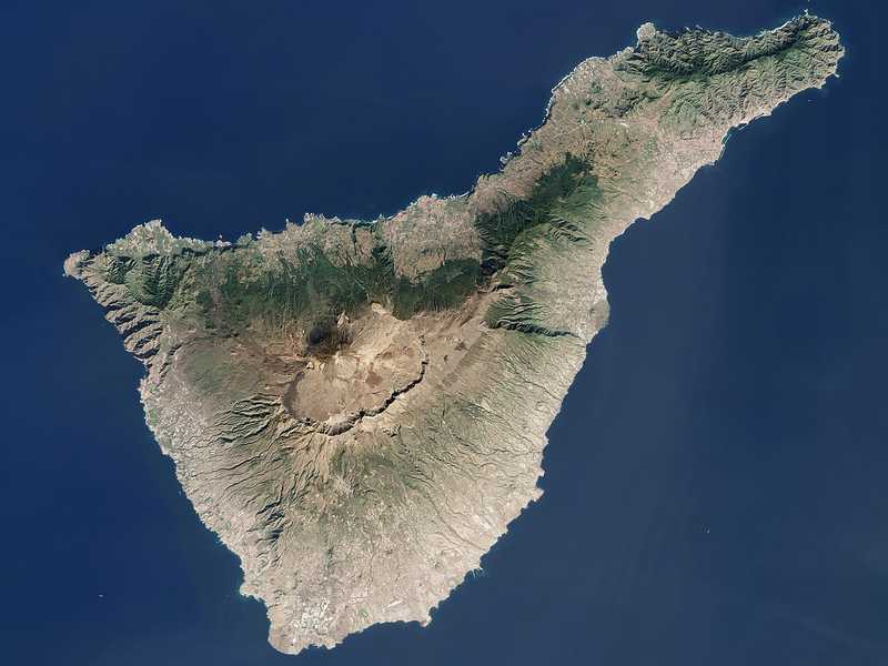 This view from space of Tenerife, the largest of Spain’s Canary Islands, vividly displays the volcanic island’s large caldera. The summit of the Teide stratovolcano reaches 3,718 m (12,198 ft) above sea level. However, much of the volcano’s impressive height is unseen below the water line. The volcano rises 7,500 m (24,606 ft) from the ocean floor, making it the third tallest volcanic structure on Earth. About 190 sq km (73 sq mi) of land around the summit are protected as part of Teide National Park. In 2007, the park was designated a UNESCO World Heritage site, joining Hawaii Volcanoes National Park as examples of the geologic processes responsible for building oceanic volcanoes. Santa Cruz de Tenerife, the island’s largest city and capital, is the large grayish area on the northeastern shore. Image courtesy of NASA.