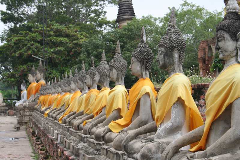 Before Bangkok was established as the royal residence, Ayutthaya was a royal palace. Today, the grounds are preserved as a shrine and historical site. A row of seated Buddha statues draped in orange and saffron robes lines the cloister gallery.