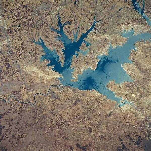 This northeast-looking view shows the Ataturk Reservoir and Dam, presently the largest man-made lake in Turkey. Located in south central Turkey on the Euphrates River, Ataturk Reservoir was completed in the early 1990&apos;s. The meandering Euphrates River (dark line) can be seen exiting the scene below the left center of the image. Smooth lake waters appear as dark blue, while wind-roughened waters appear light blue. The light area to the west of the dam (left center) is where rocks were quarried for the construction of the dam. Photo courtesy of NASA.