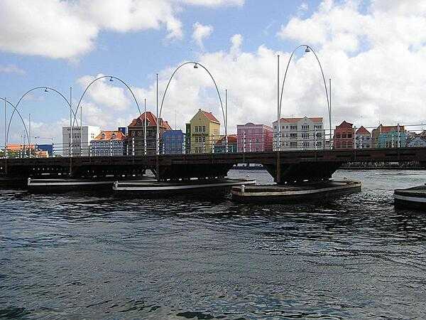 Spanning St. Anna Bay, the Queen Emma floating bridge at Willemstad, Curacao is the oldest permanent wooden pontoon bridge in the world. Known as the “Swinging Old Lady,” the bridge connects Willemstad's two halves, Punda and Otrobanda, and was named after Emma of Waldeck and Pyrmont, who was queen consort of the Netherlands during its construction in 1888. The bridge is supported by 16 pontoon boats and laterally swings open to allow ships to enter and leave the bay. With the opening of the Juliana Bridge in 1974, the Emma Bridge became solely a pedestrian bridge closed to all vehicles.