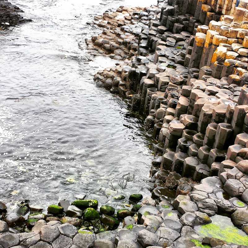 The Giant's Causeway (Irish: Clochán an Aifir) is a site of about 40,000 interlocking basalt columns, the result of an ancient volcanic eruption. As the lava cooled, contraction occurred in a pattern similar to that of drying mud, with the cracks propagating in a generally hexagonal pattern and downward, leaving pillarlike structures. The unique geological formation is located in County Antrim on the north coast of Northern Ireland, about 5 km (3 mi) northeast of the town of Bushmills.