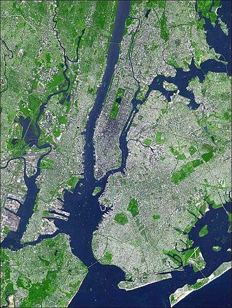 This false-color satellite image shows greater New York City. The Island of Manhattan is jutting southward from top center, bordered by the Hudson River to the west and the East River to the east. (North is straight up in this scene.) In the middle of Manhattan, Central Park appears as a long green rectangle running roughly north-south with a large lake in the middle. Also visible are parts of Staten Island (bottom left corner) and Long Island (lower right). Photo courtesy of NASA.