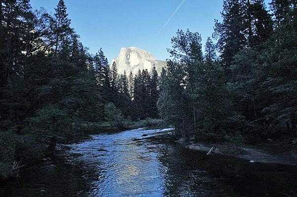 This image from Sentinel Bridge shows Yosemite Valley at sunset. Half Dome, the brightly lit rock formation in the background, is one of the last places in the valley to receive sunlight as the day ends.
