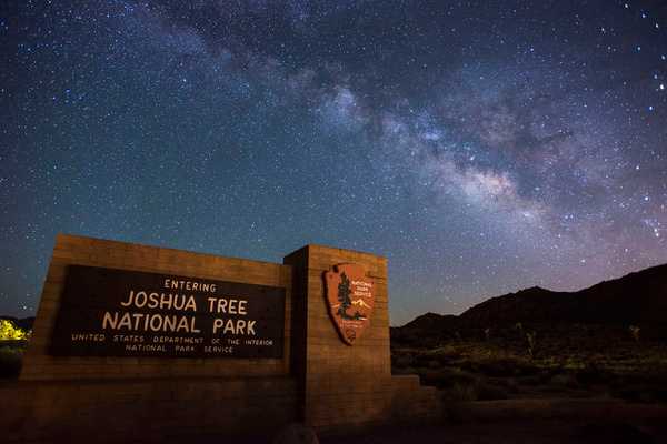 The Milky Way galaxy arches over the entrance sign to Joshua Tree National Park in California. Photo courtesy of the US National Park Service/ Lian Law.